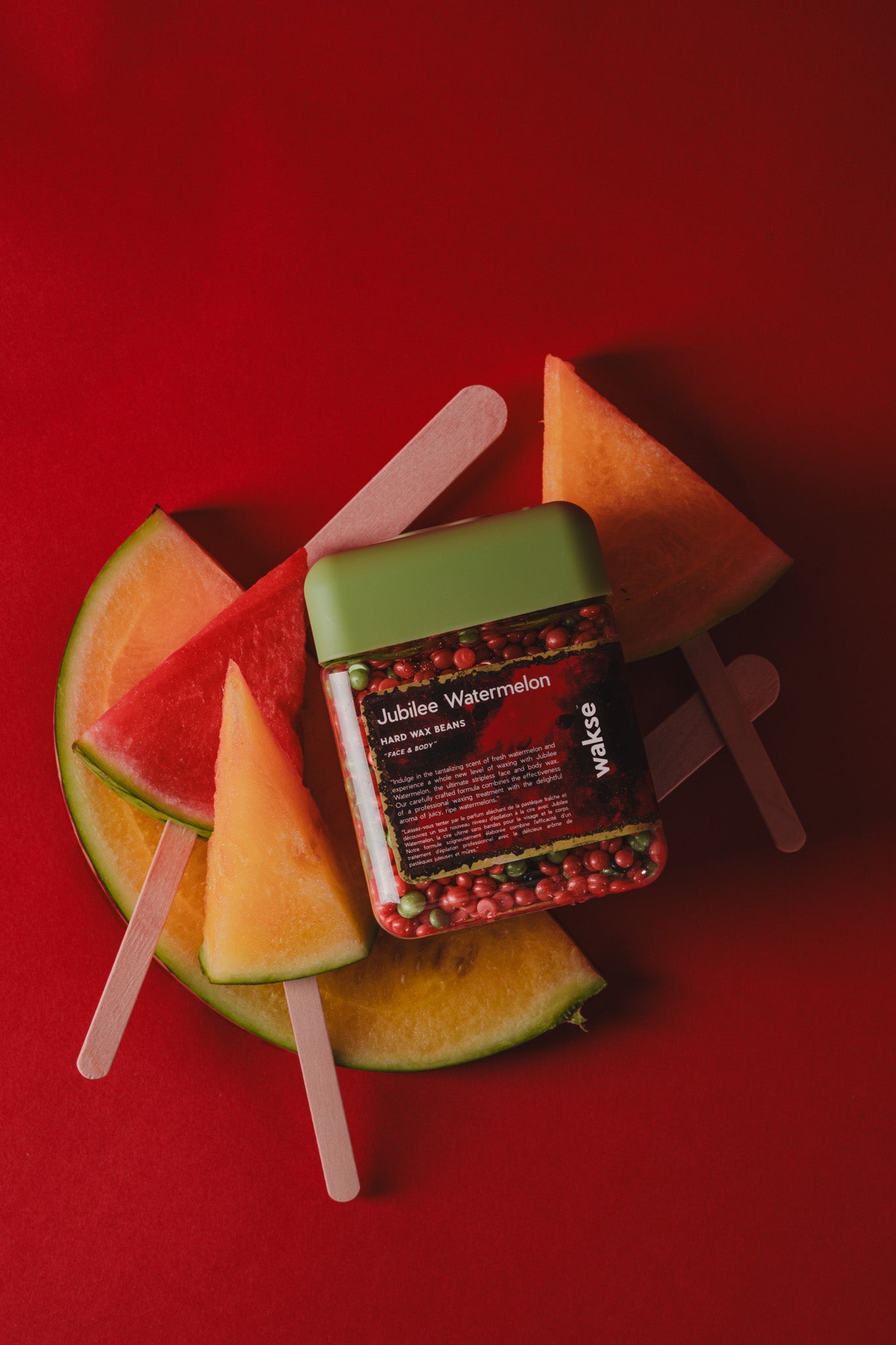waksewatermelon slices and popsicle sticks on a red background