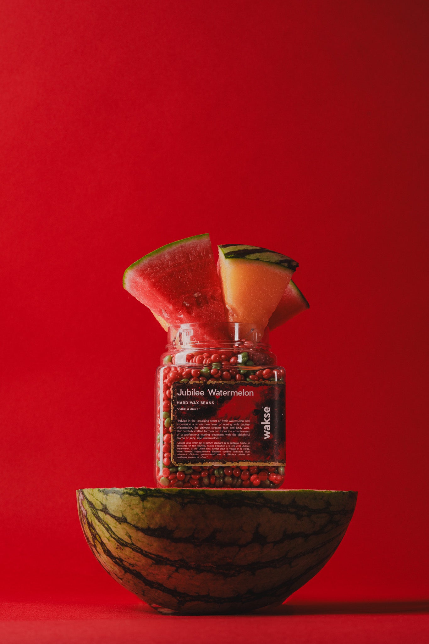 wakse Glass jar filled with red berries on a watermelon slice against a red background