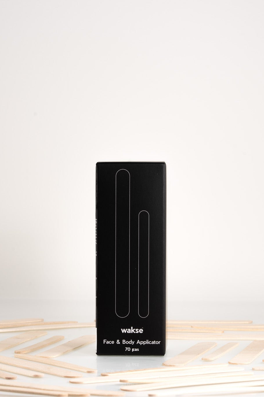 Black packaging box for face and body wax applicator set with wooden sticks around it